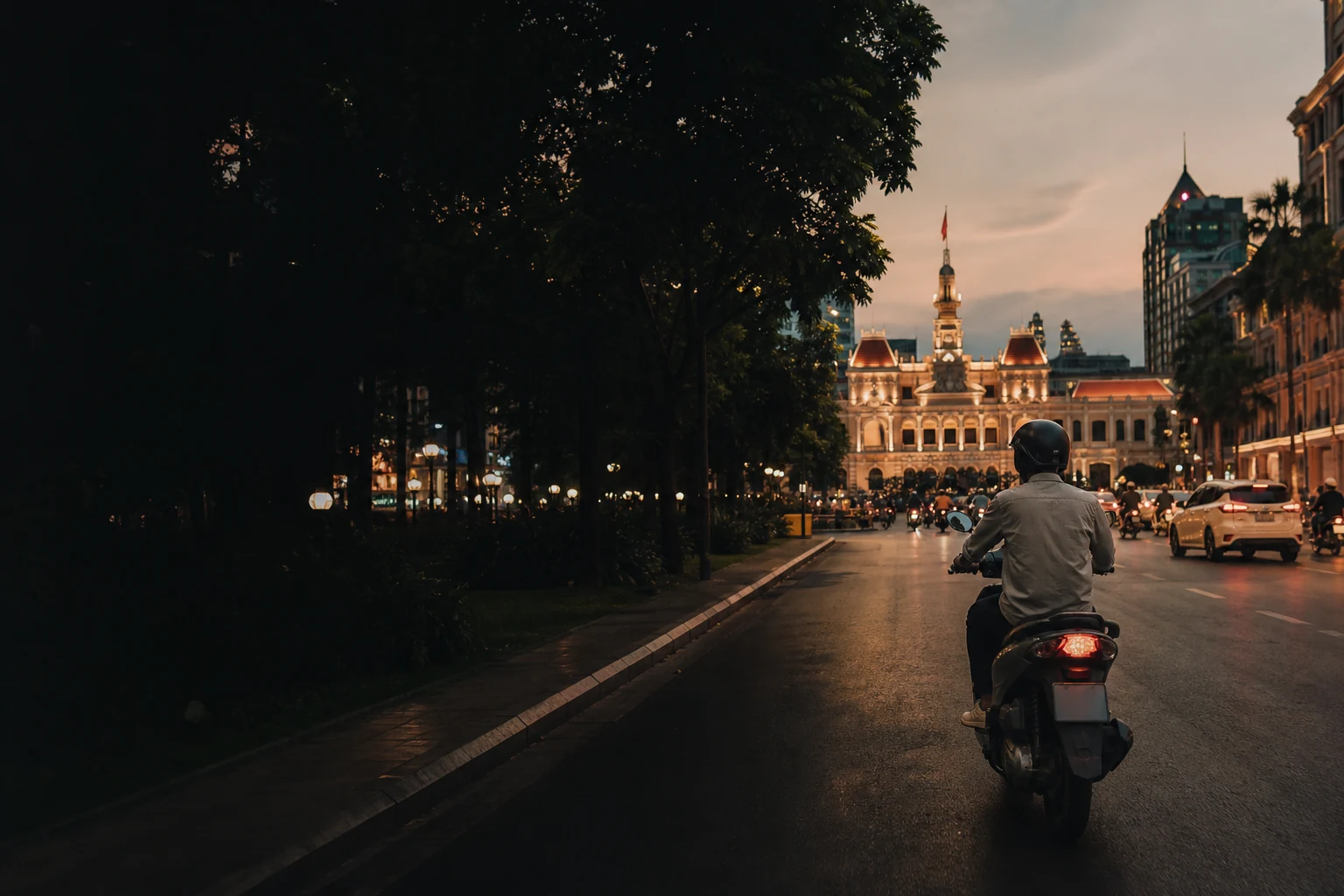 Helmeted scooter rider crossing a lit District 1 street near Ho Chi Minh City Hall