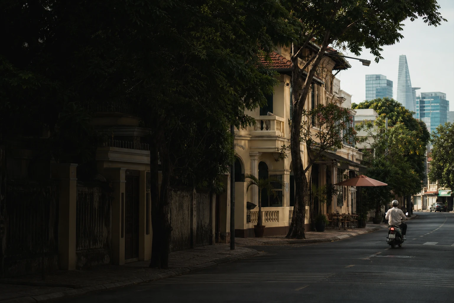Helmeted scooter rider passing a tree-lined heritage street in District 3, Ho Chi Minh City